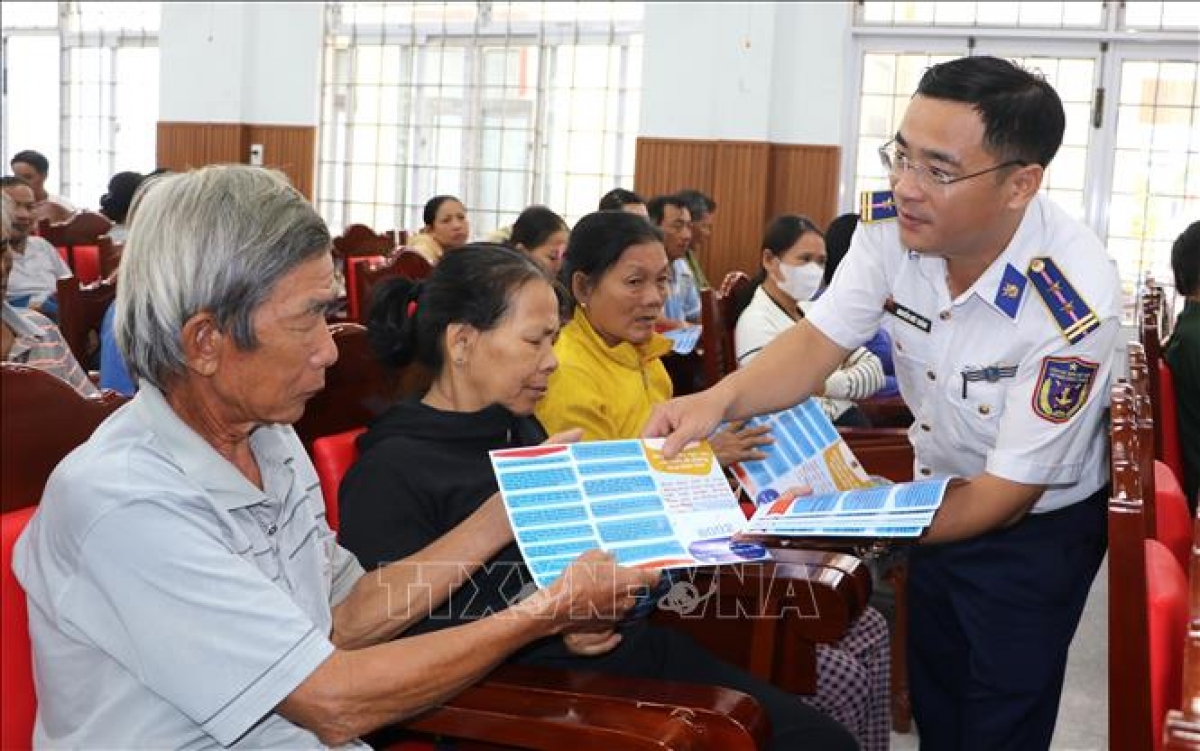 Coast Guard officers distribute leaflets on combating IUU fishing to local fishermen. (Photo: Dinh Huong/VNA)
