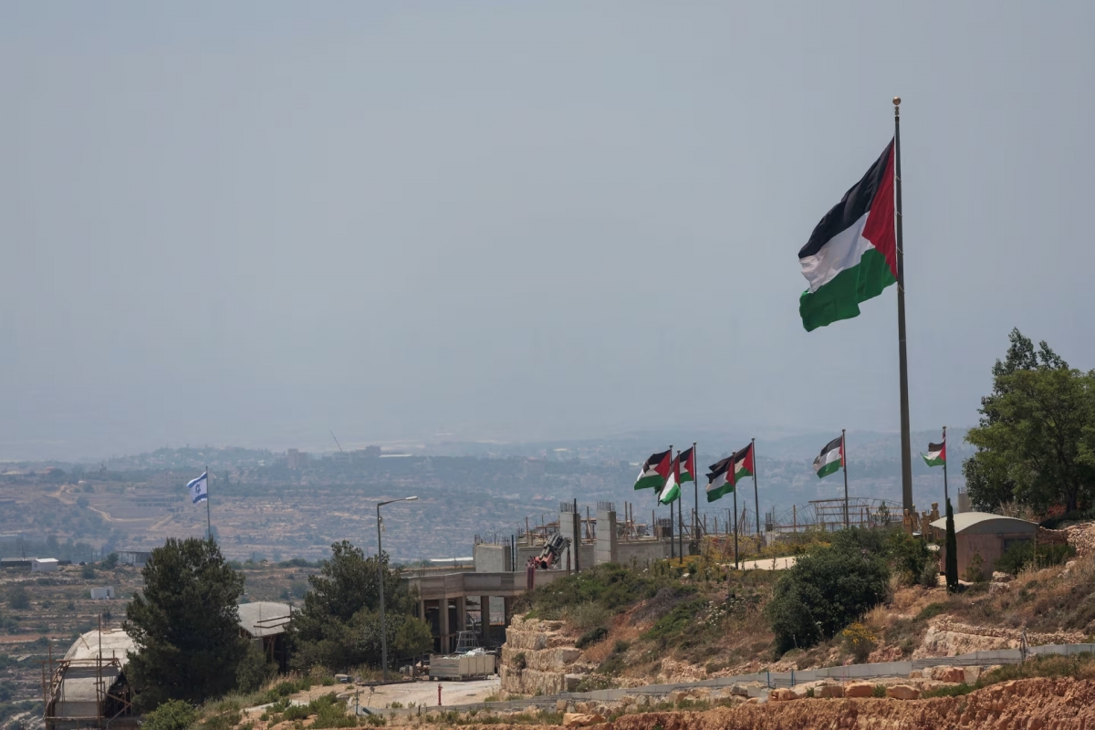 Bendera Israel berkibar di zona pemukiman baru Israel , di belakang bendera Palestina dekat Ramallah di Tepi Barat yang diduduki Israel, 1 Juni 2026. Foto: REUTERS/Mohammed Torokman