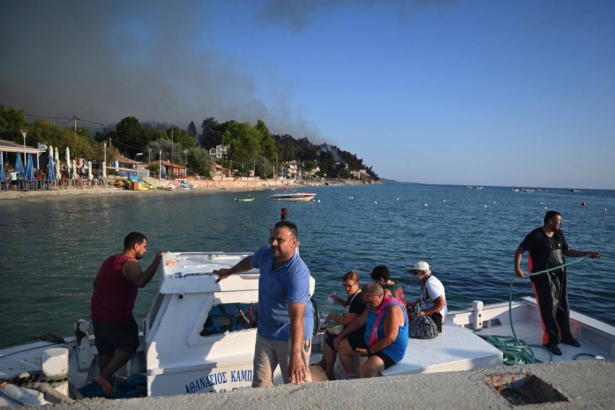 Des touristes sont évacués par un bateau de pêche lors d'un incendie de forêt à Siviri, sur la péninsule de Chalcidique, dans le nord de la Grèce, le 13 août 2026. Photo: AP/Giannis Papanikos