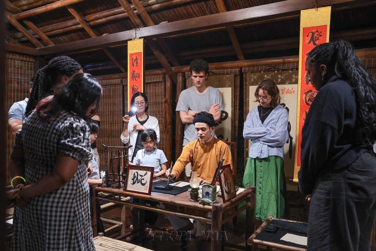 Tourists watch calligraphers demonstrate their skills in a traditional cultural setting during a night tour of the Temple of Literature in Hanoi. Photo: Pham Tuan Anh/VNA