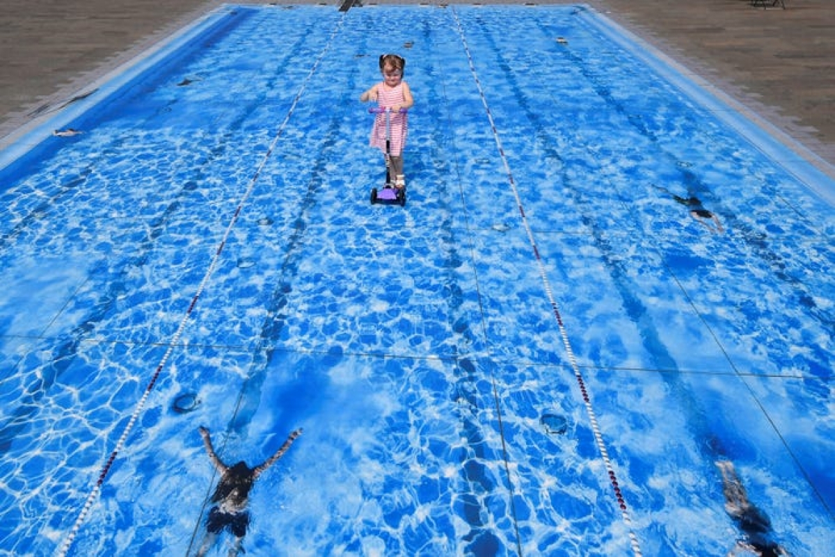 Although viewers may think this image shows a child riding a scooter on a pool, it's really just a piece of art on the floor on display in London. (Photo: Reuters/Toby Melville)